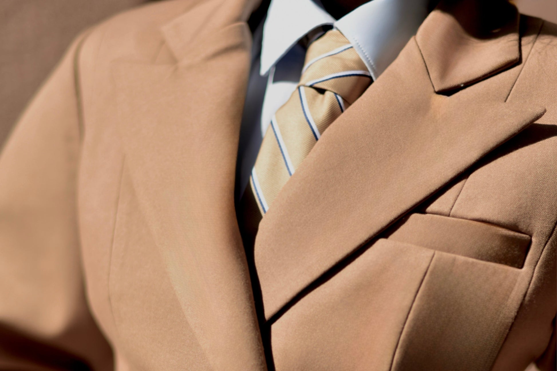Close-up of a person wearing a beige suit with a patterned tie.